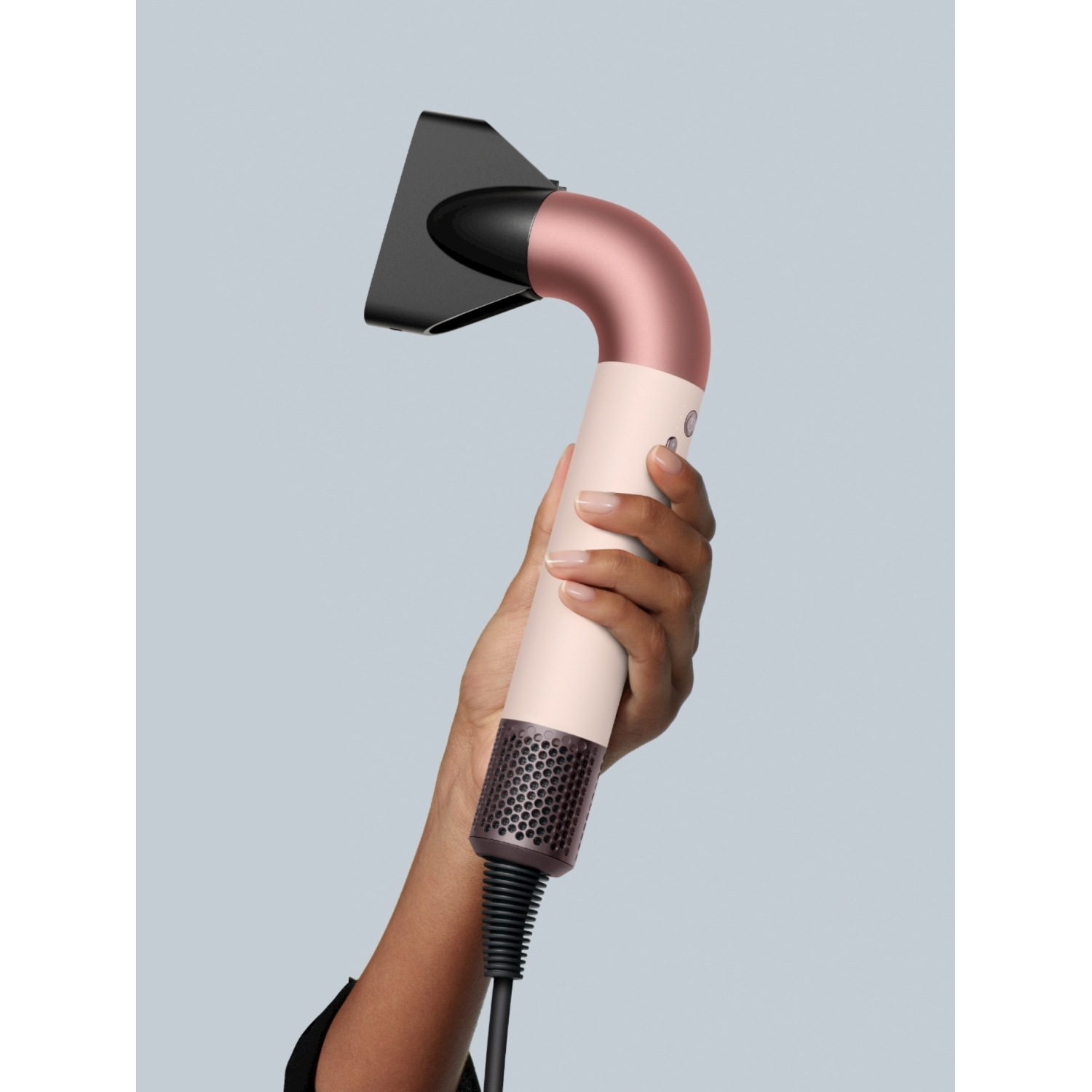 Eine Hand hält einen roségoldenen Haartrockner mit weißem Griff.