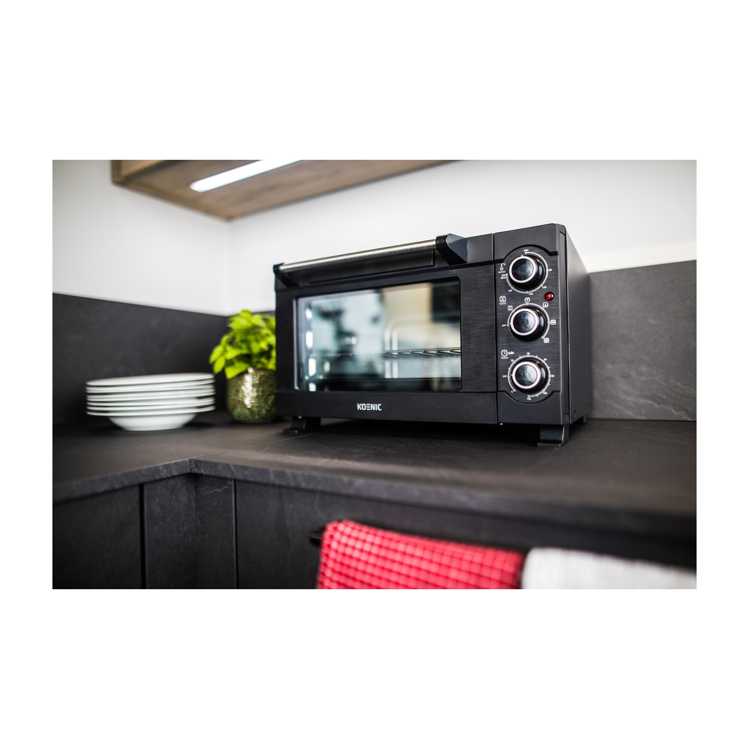 Un horno de sobremesa negro en una encimera de cocina con platos y una planta cerca.
