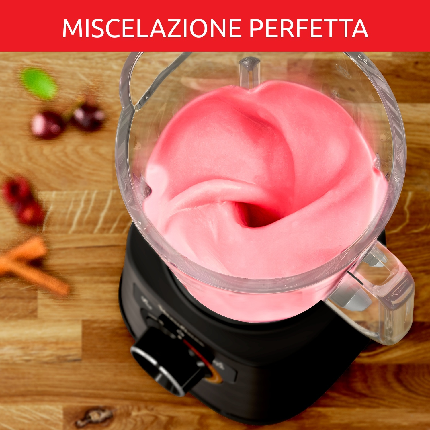 Un frullatore con impasto rosa, con ciliegie e carote su legno.