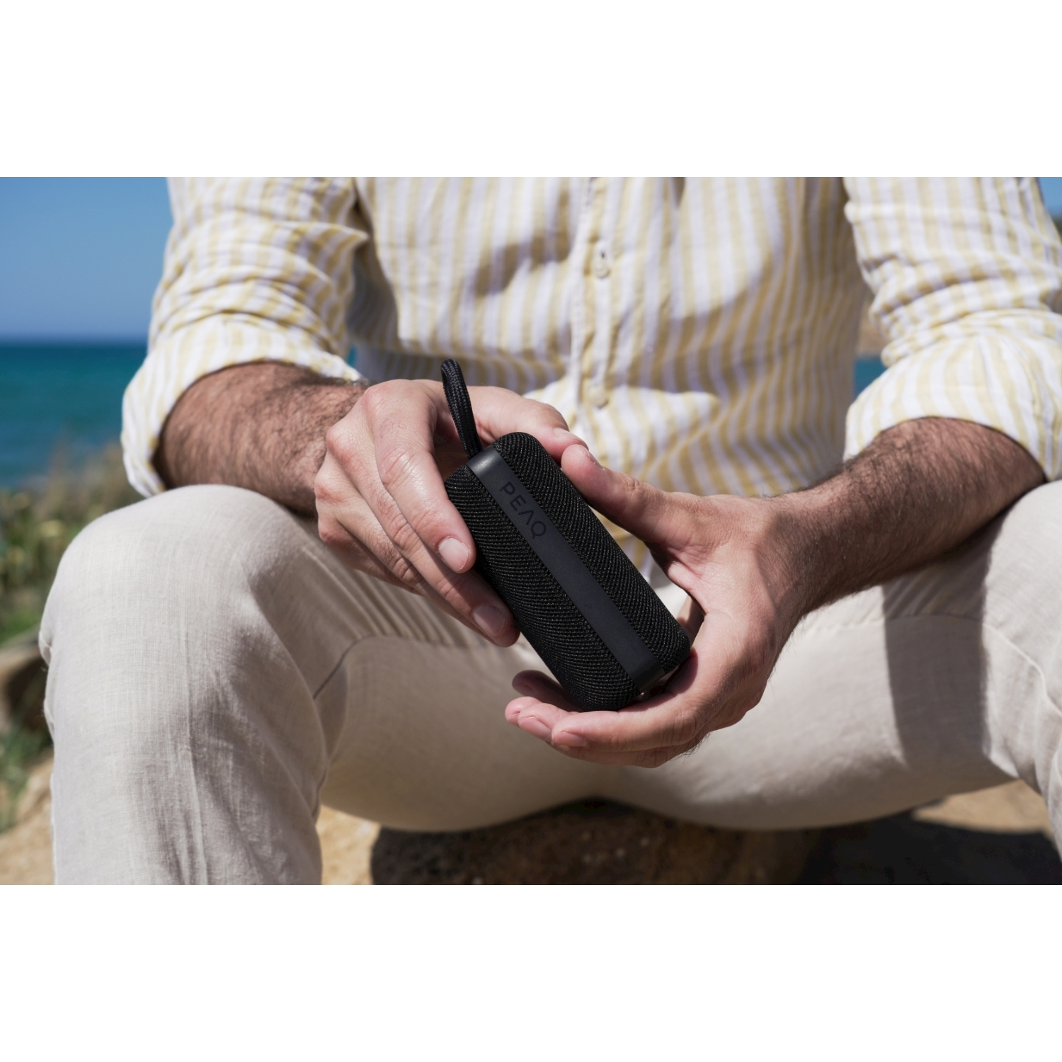 Mann hält schwarzen Lautsprecher am Strand bei Sonne.
