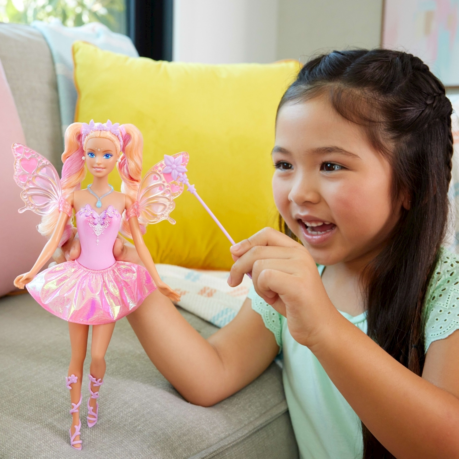 Ein Mädchen hält eine Barbie-Puppe mit Flügeln und Zauberstab im Wohnzimmer.