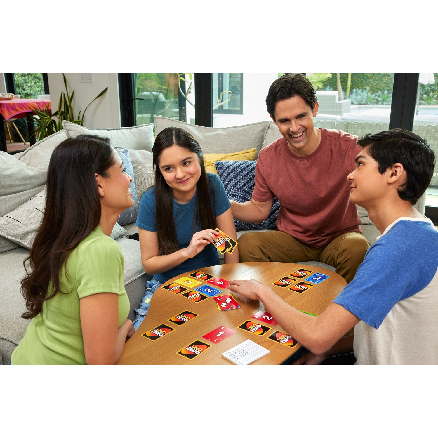 Vier mensen spelen UNO aan een ronde tafel in een woonkamer.