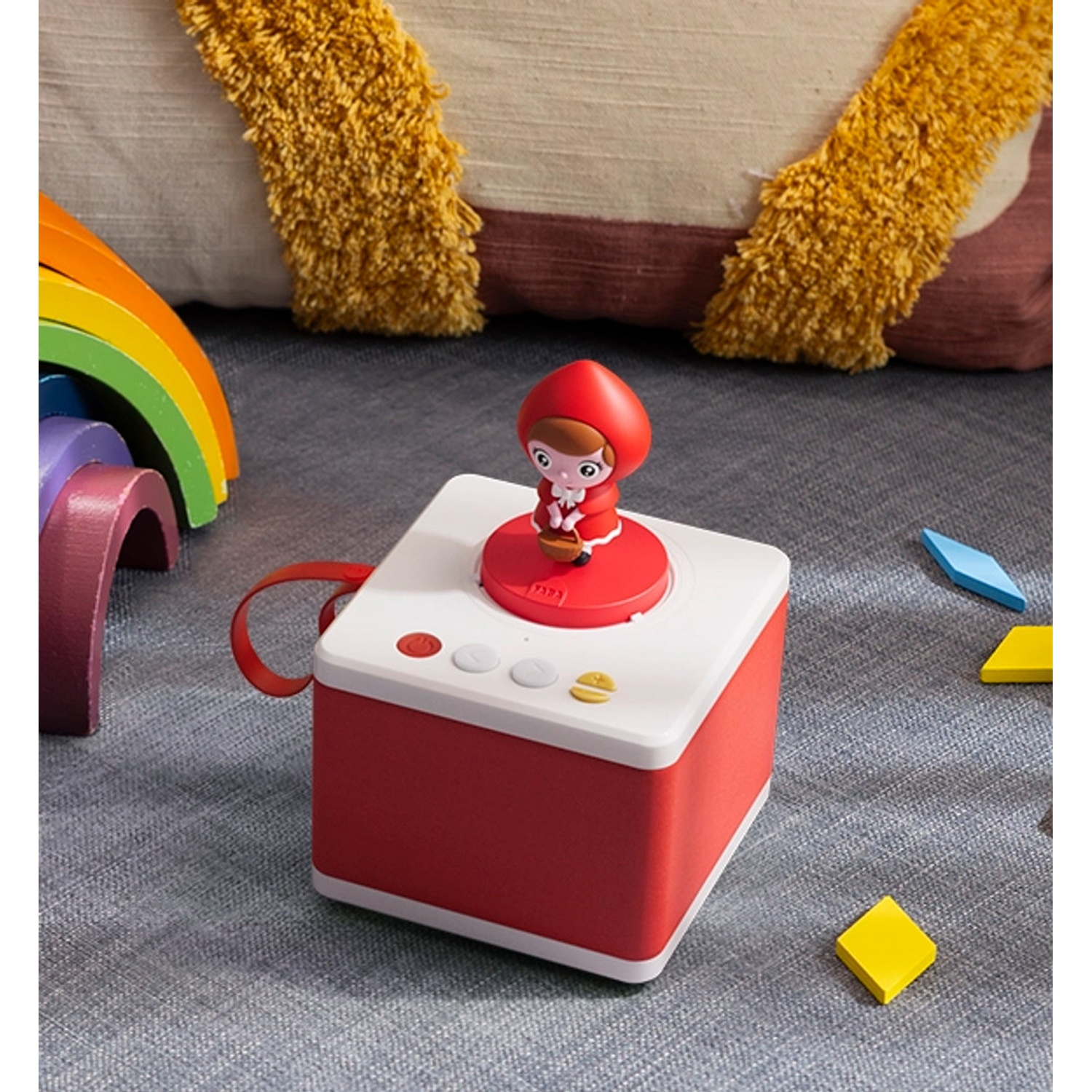Scatola rossa con figura di Cappuccetto Rosso, arcobaleno di legno e blocchi colorati su tappeto grigio.