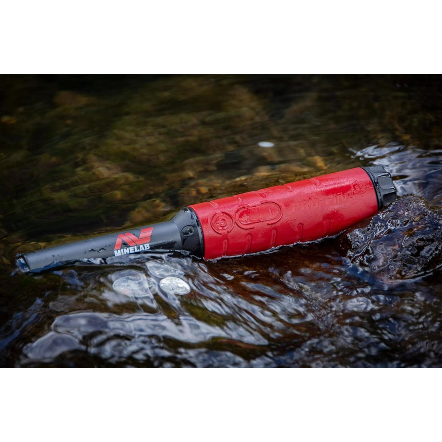 Ein roter Minelab Metalldetektor liegt in seichtem Wasser mit Münzen.