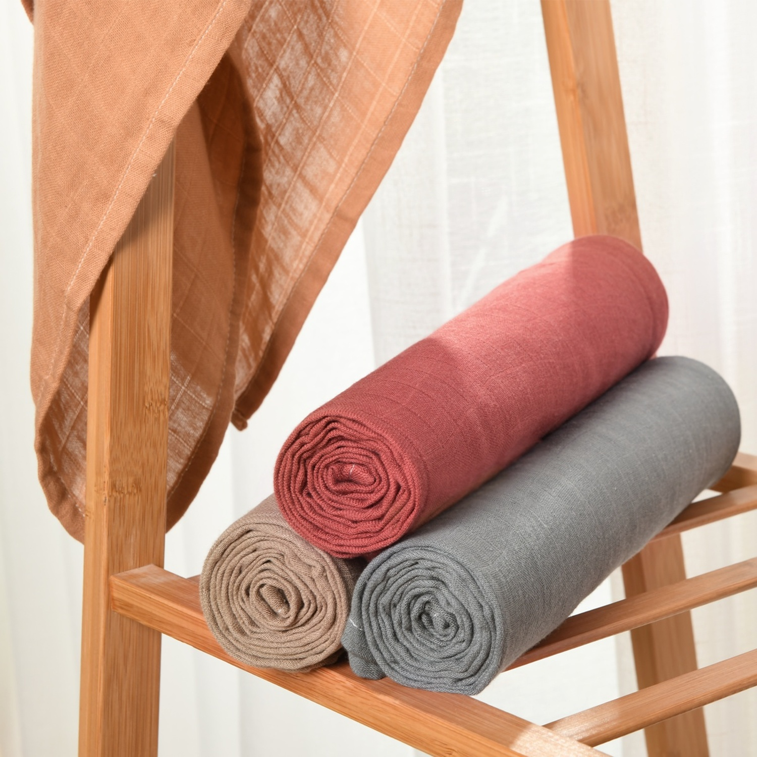 Rotoli di tessuto marrone, rosso e grigio su un supporto di legno.