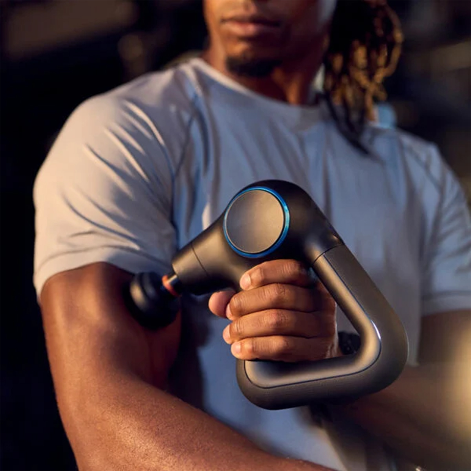 Osoba trzyma czarny pistolet do masażu na bicepsie. Pistolet ma niebieski pierścień.