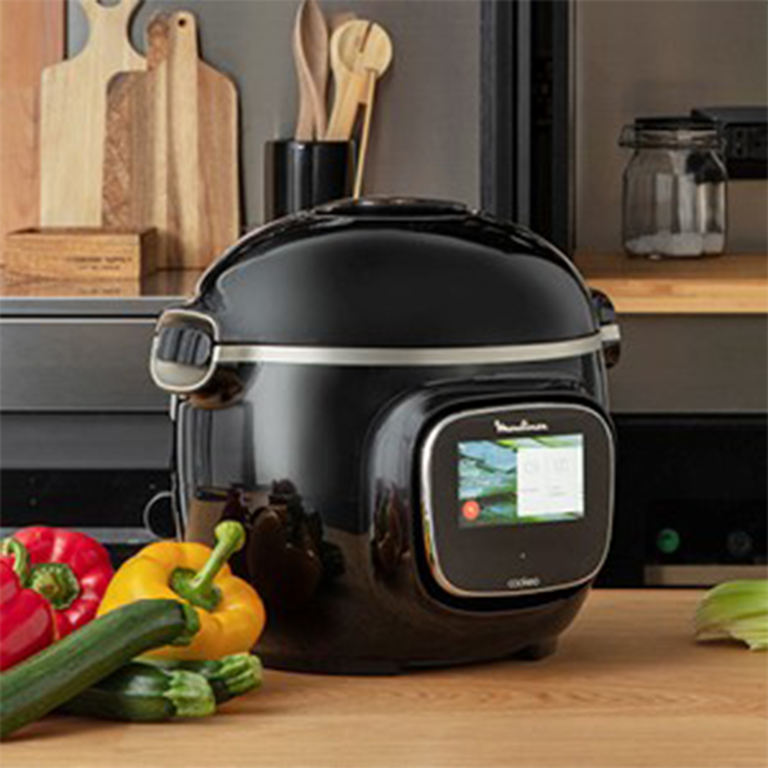 Un elettrodomestico da cucina nero su un tavolo di legno con verdure e utensili.