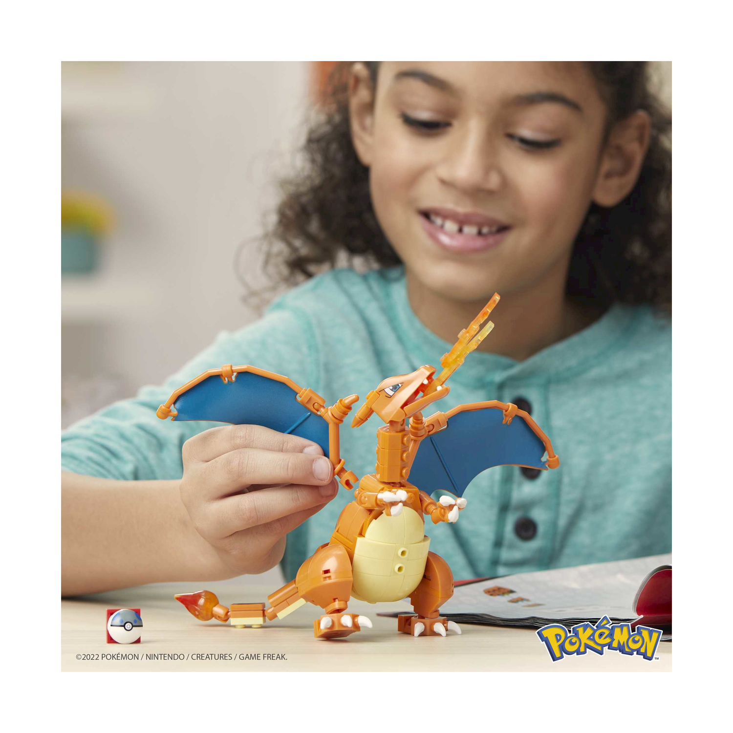 Dziecko buduje pomarańczową postać Pokémona z niebieskimi skrzydłami z klocków.