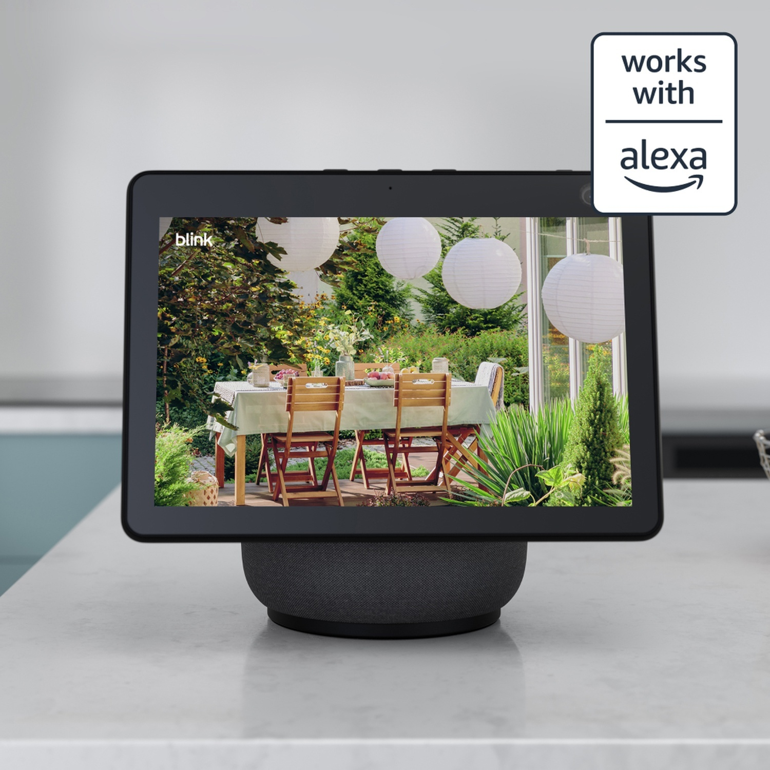 Ein Tablet zeigt eine Gartenansicht mit Tisch und Stühlen. Oben rechts steht 'Works with Alexa'.