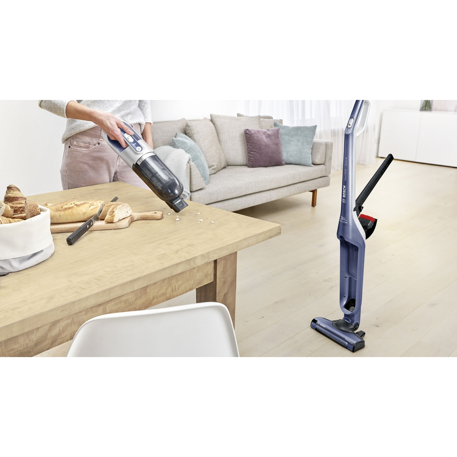Una persona usa una aspiradora azul de mano sobre una mesa de madera con pan.