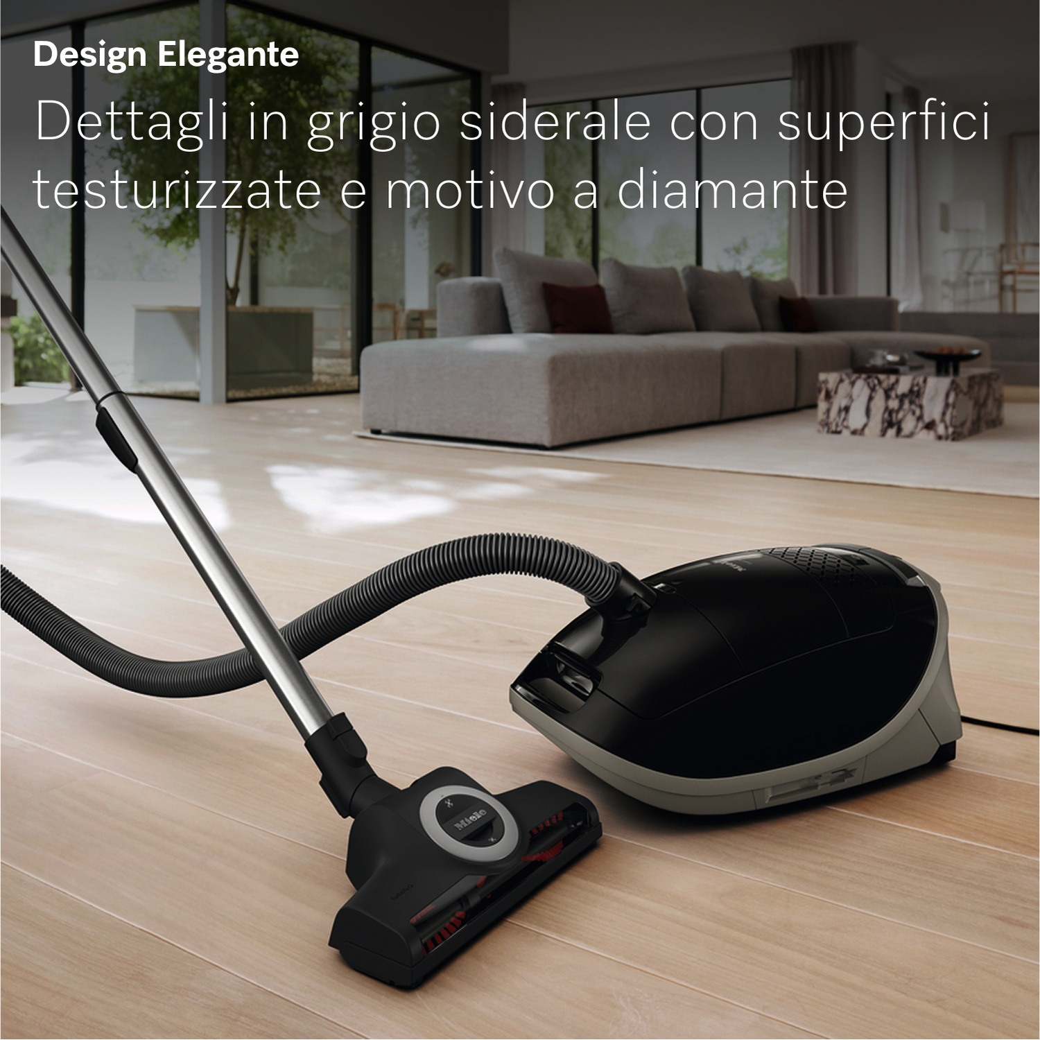 Un aspirateur Miele noir avec un tube argenté repose sur un plancher en bois.