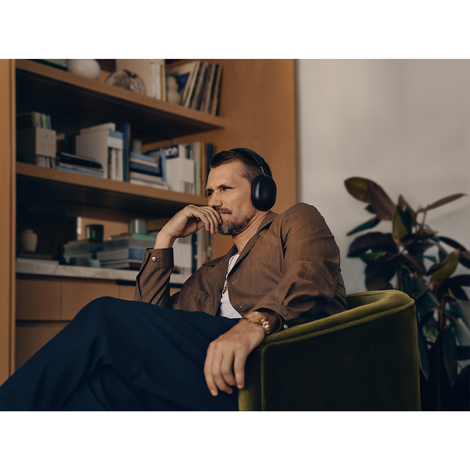 Mężczyzna w słuchawkach siedzi zamyślony w zielonym fotelu, za nim regał z książkami.