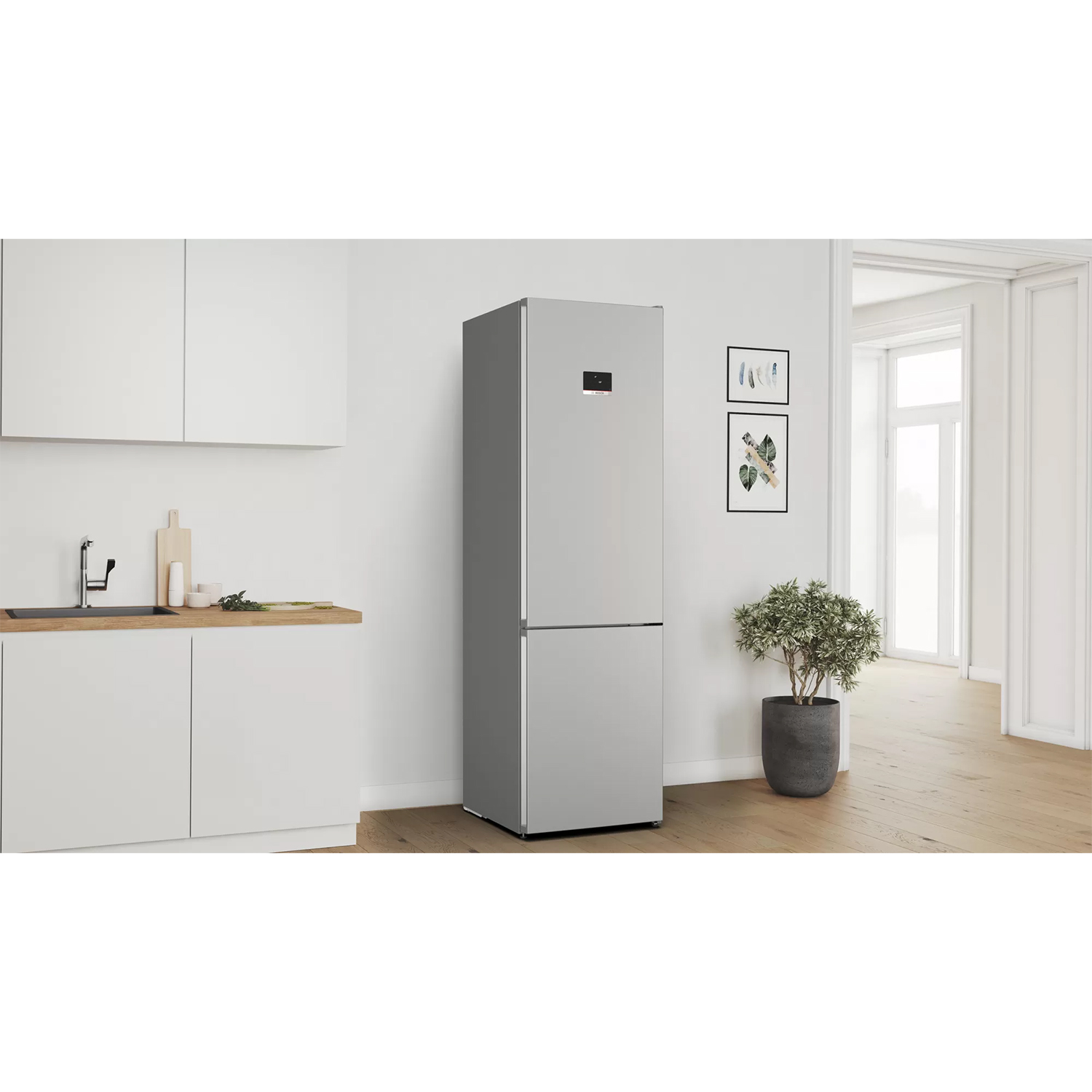 Un refrigerador plateado se encuentra en una cocina moderna junto a una encimera con fregadero y planta.