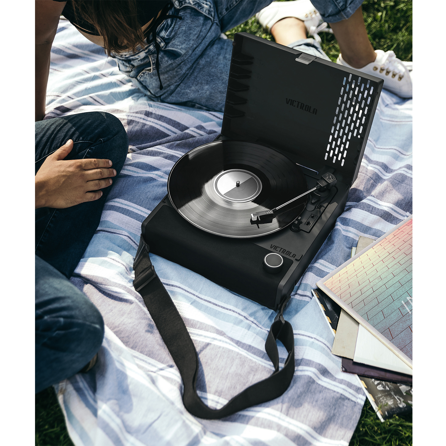 Tocadiscos negro sobre manta con vinilo y personas en la hierba.