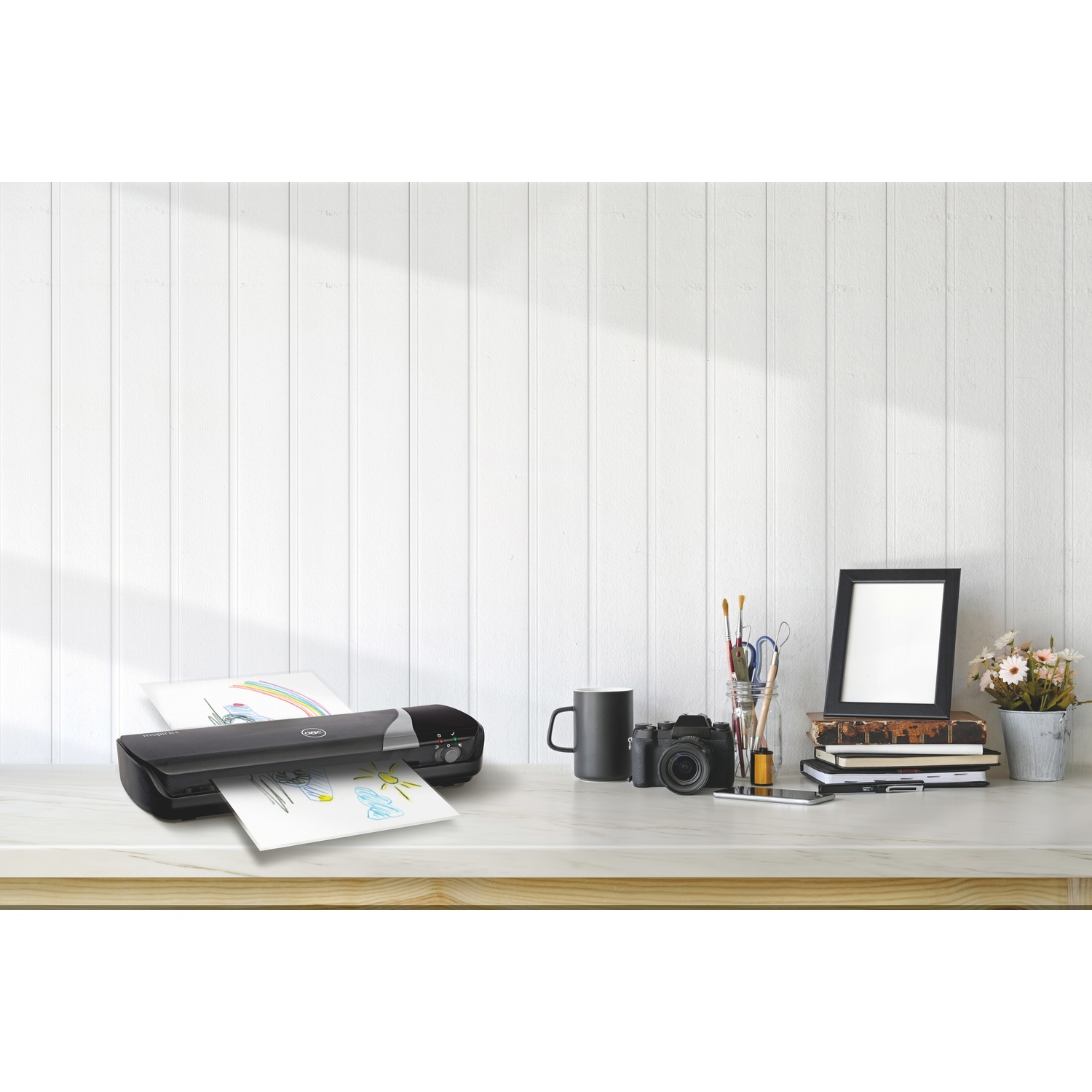Una plastificatrice nera con carta, una fotocamera e una cornice su una scrivania.