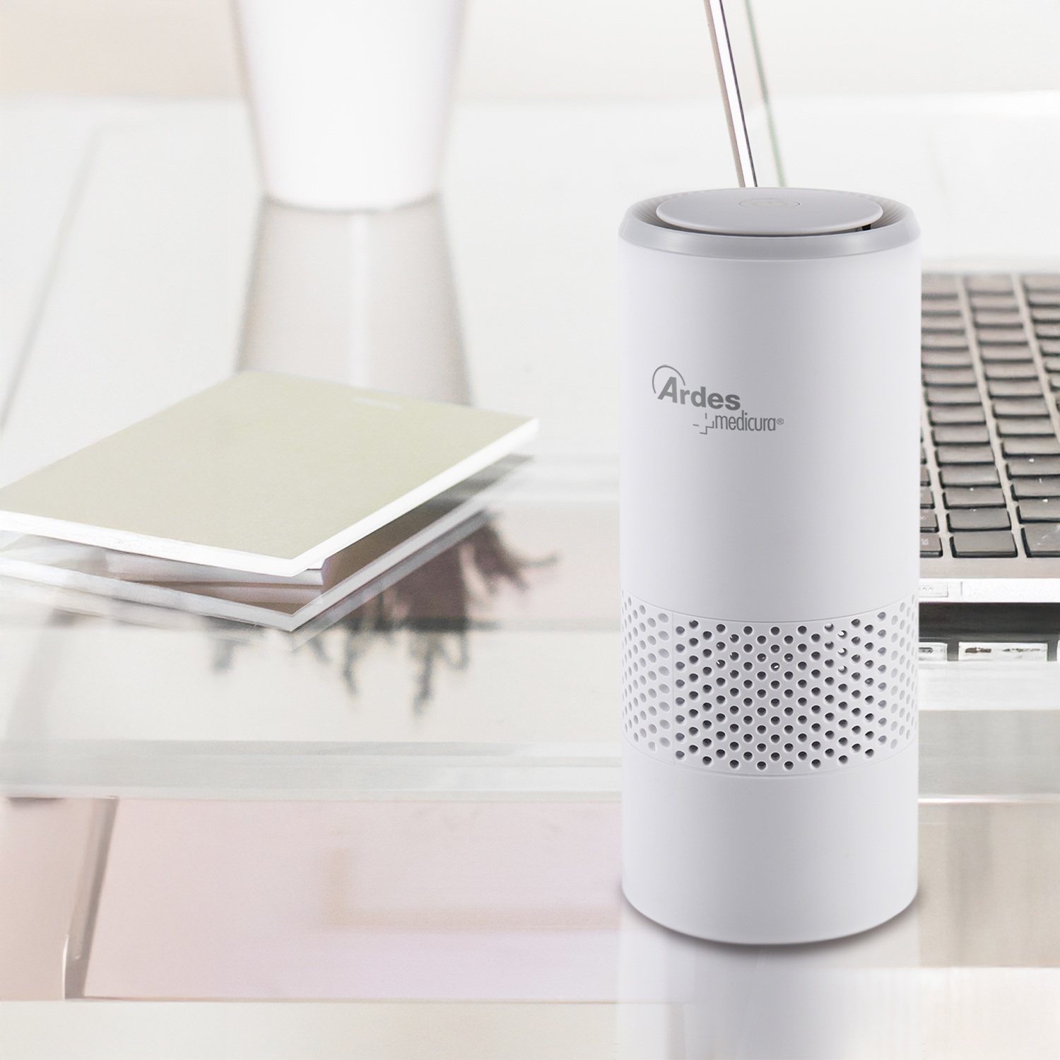 Un purificatore d'aria bianco è su una scrivania accanto a un laptop e quaderni.