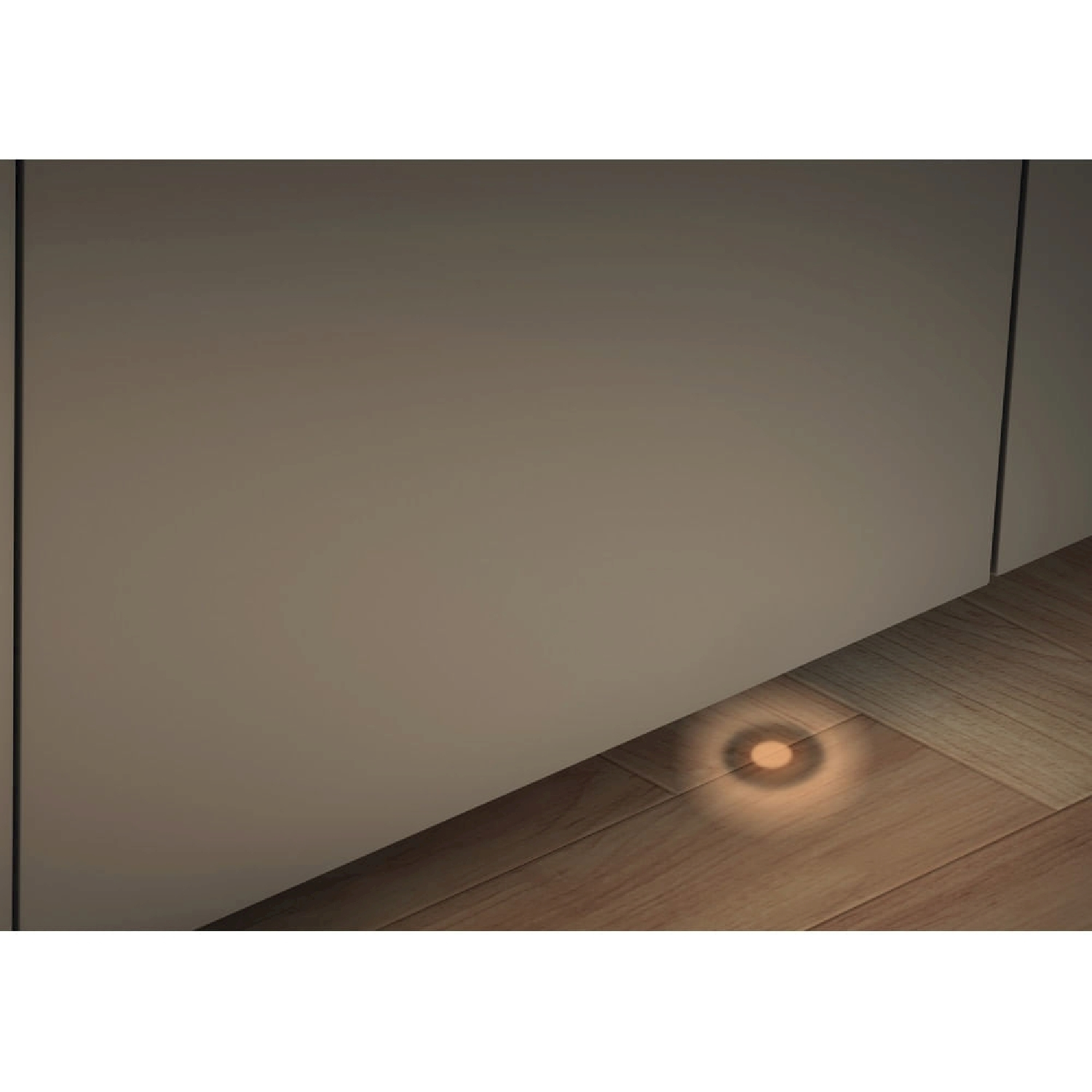 Una piccola luce rotonda brilla su un pavimento in legno accanto a un muro.