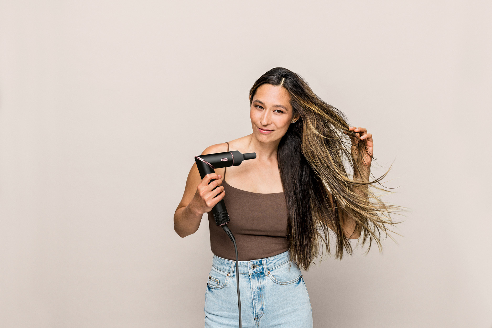 Vrouw met haardroger en lang haar tegen effen achtergrond.