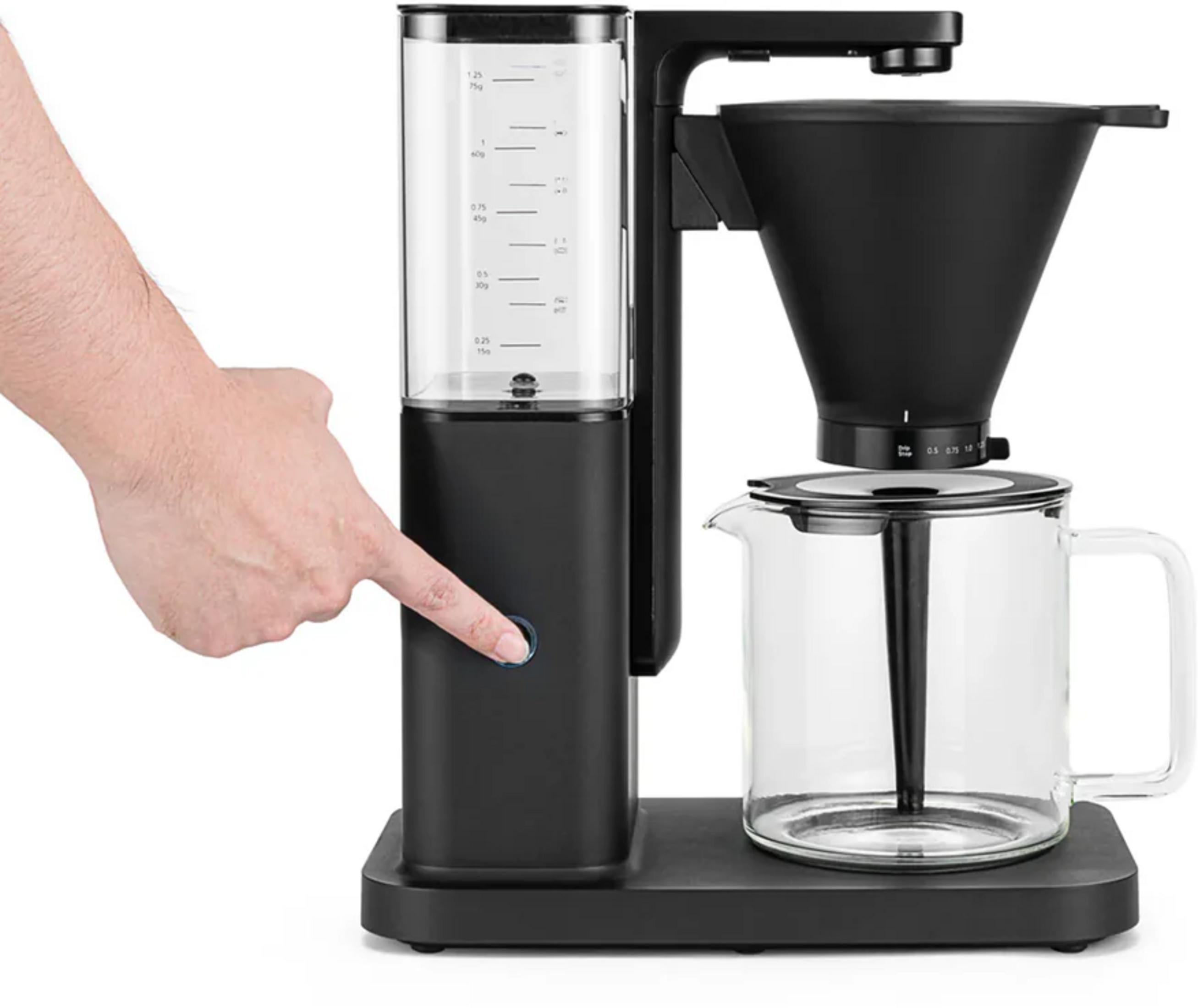 Una mano preme un pulsante su una macchina da caffè nera con caraffa di vetro.
