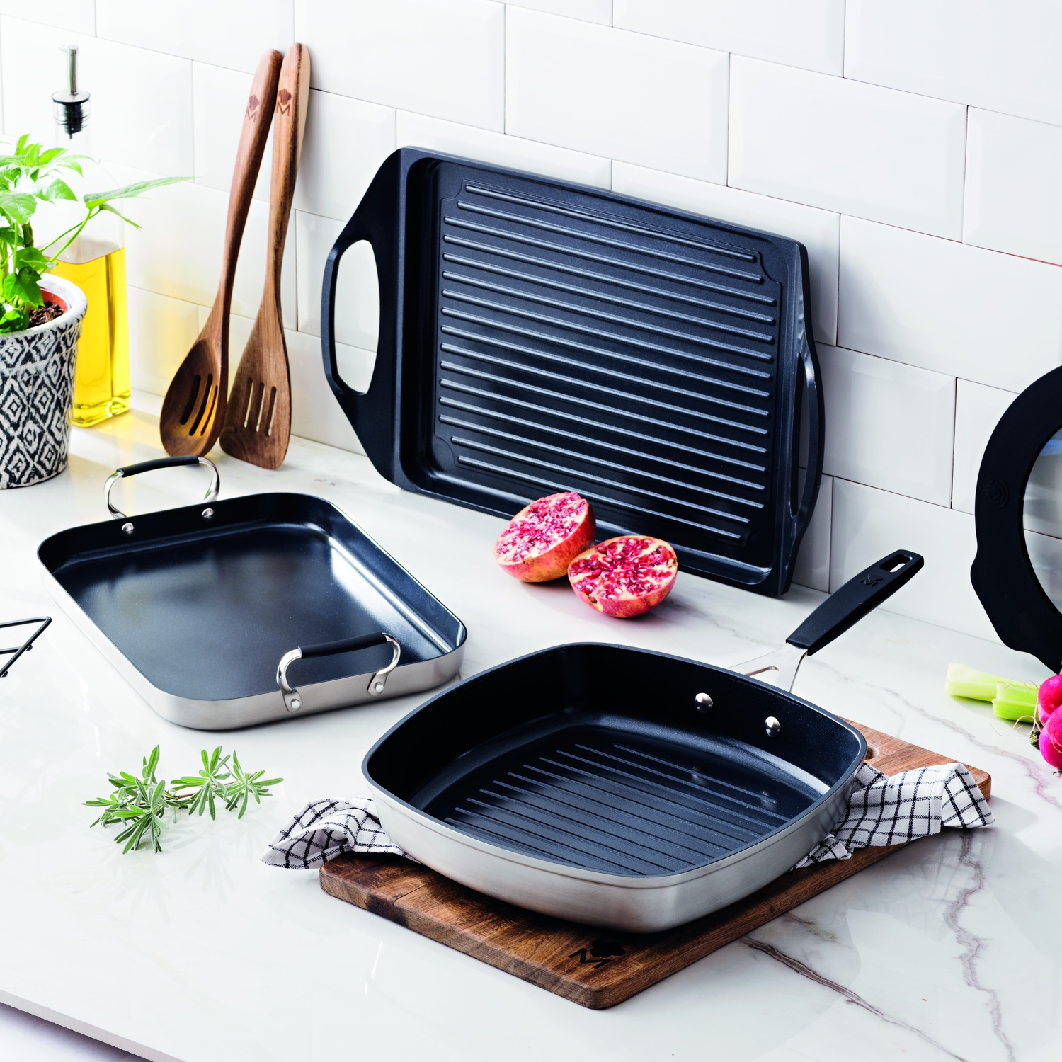 Sarten grill, utensilios de cocina y granadas en una encimera de mármol.