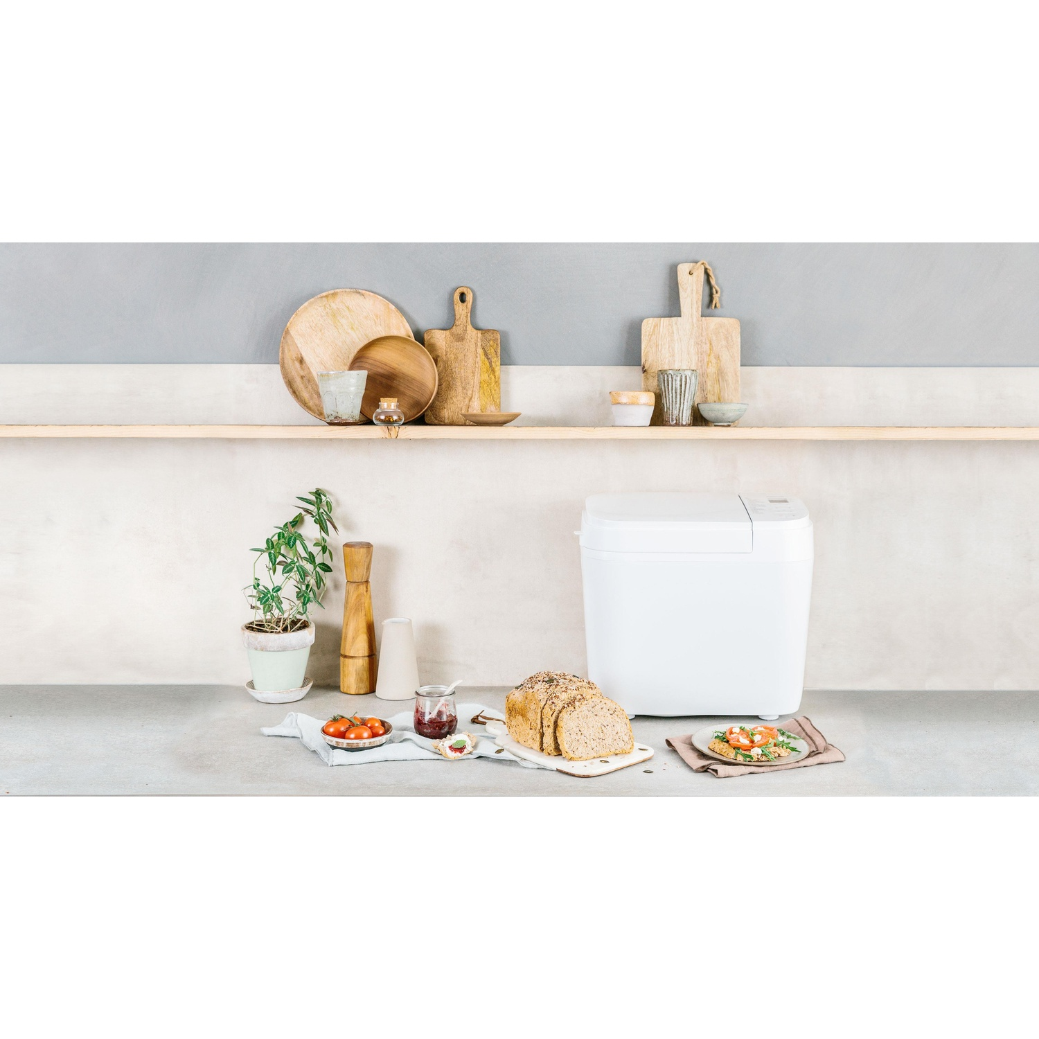 Een witte broodbakmachine met brood, toast en tomaten op een aanrecht.