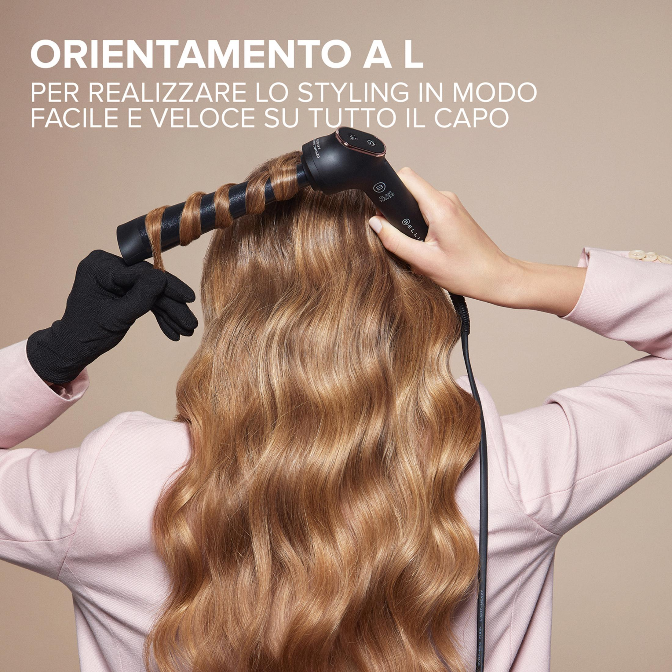 Persona con capelli biondi usa un arricciacapelli nero. Indossa un blazer rosa.