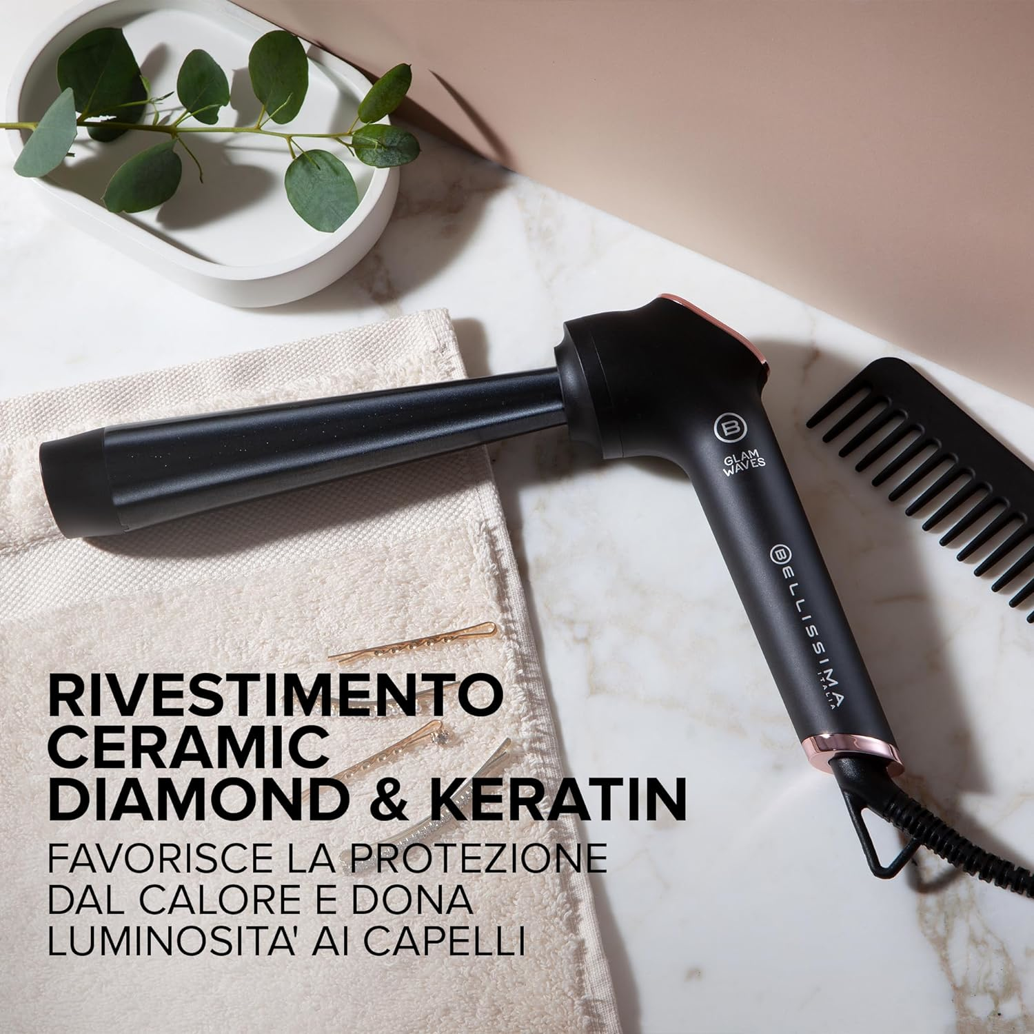 Arricciacapelli nero con accenti oro rosa, pettine, asciugamano e forcine su marmo.