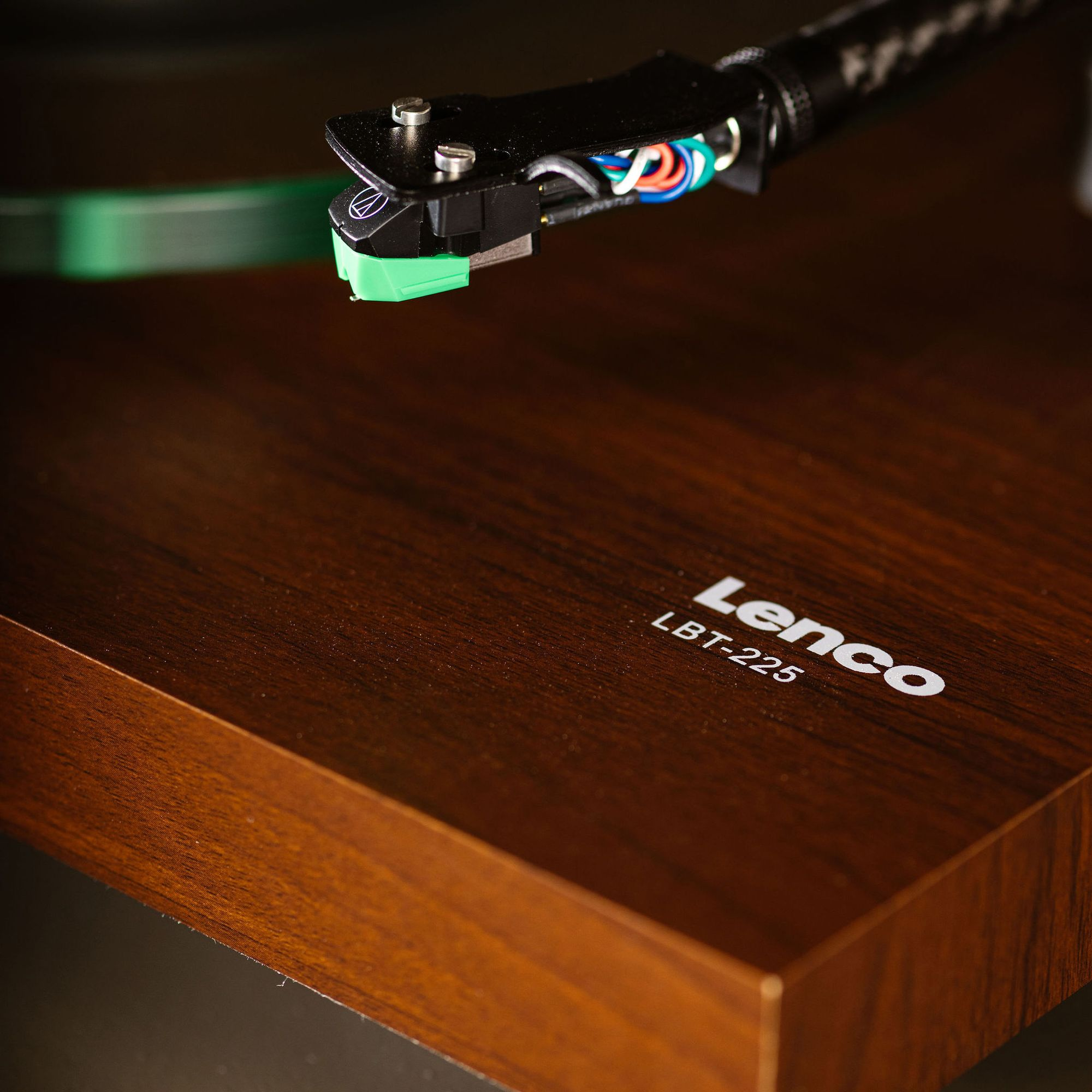 Ramię gramofonu z zieloną igłą na gramofonie z drewnianym usłojeniem.