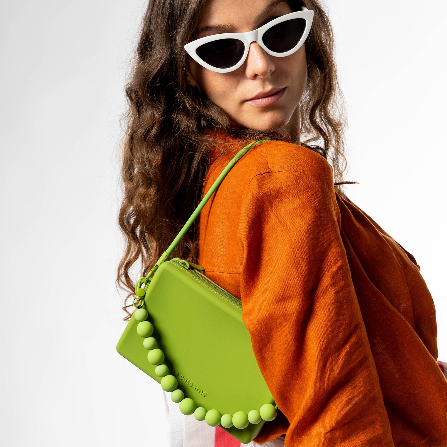 Mujer con pelo castaño rizado, gafas de sol blancas ojo de gato, camisa naranja y bolso verde de cuentas.