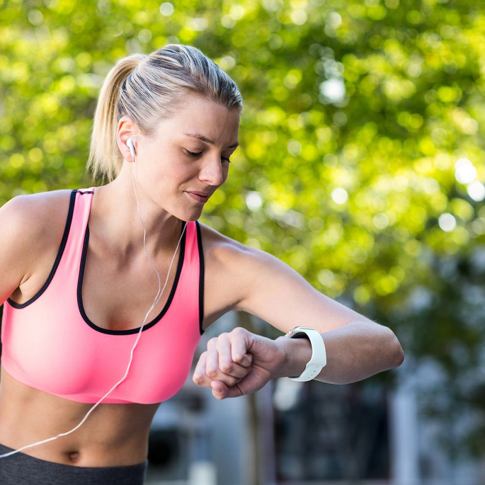 Eine Frau mit blondem Zopf in Sportkleidung schaut auf ihre Smartwatch.