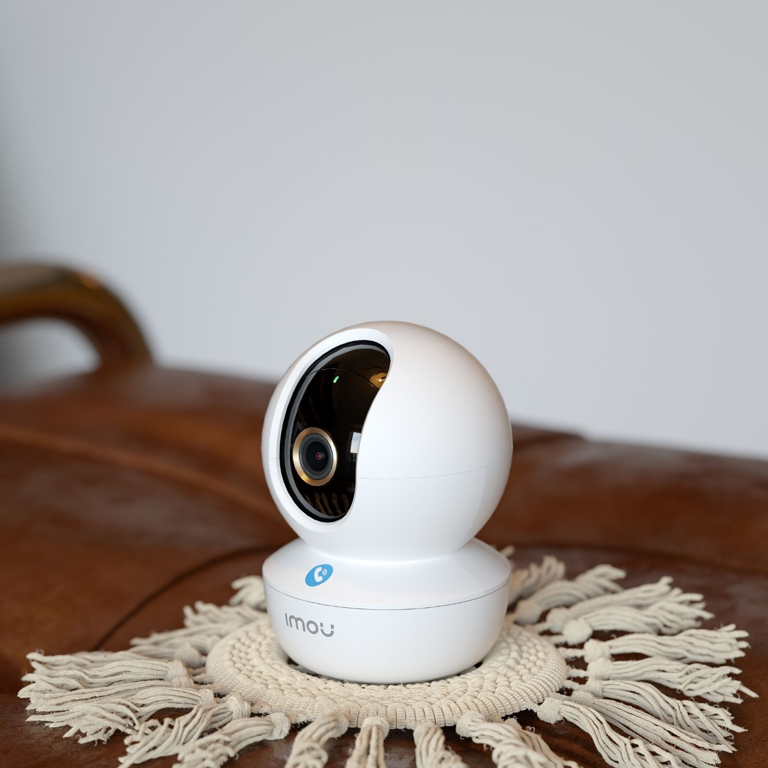 Biała kamera bezpieczeństwa z niebieskim logo na brązowej skórze.