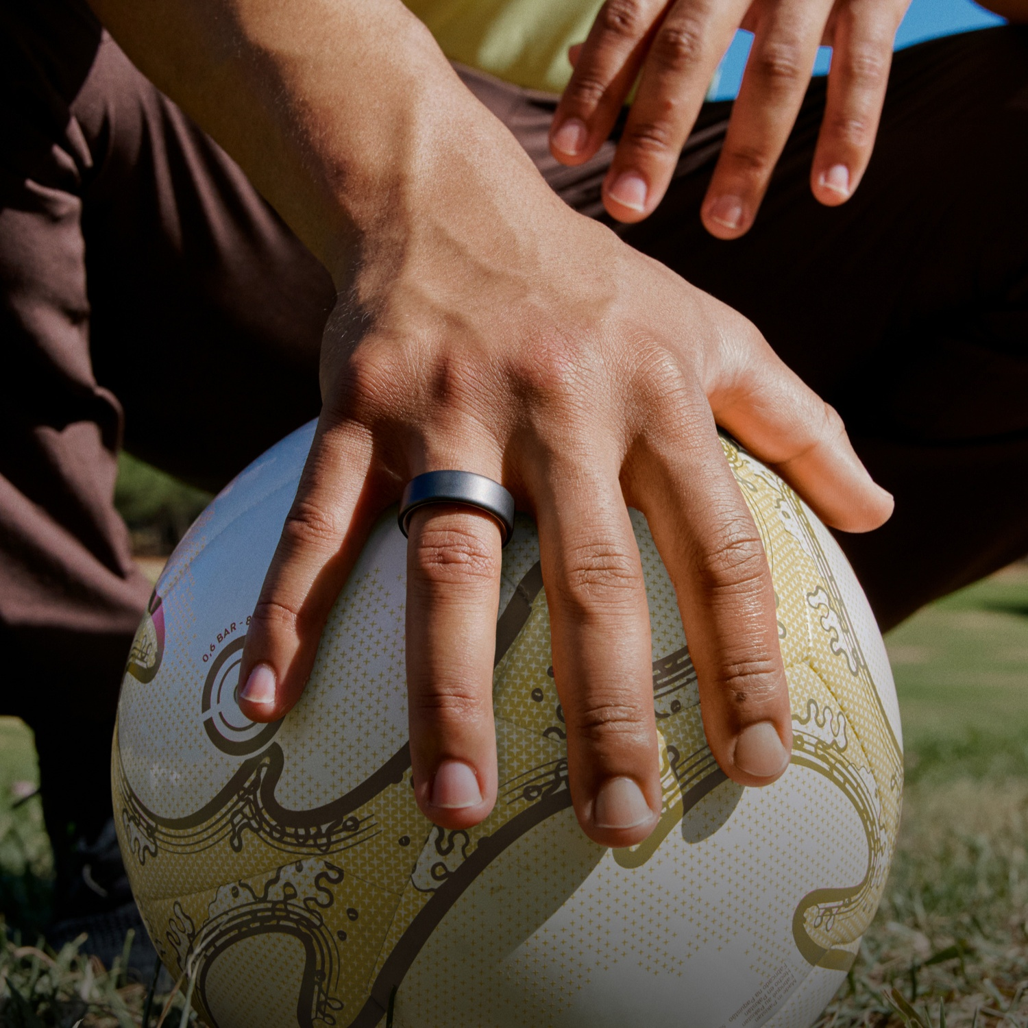 Eine Hand mit Ring liegt auf einem Fußball mit gelben Mustern.