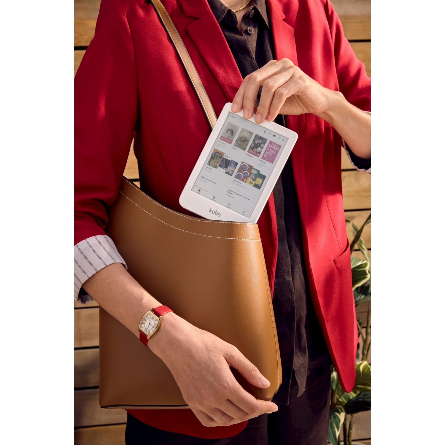 Kobieta w czerwonej marynarce i brązowej torbie trzyma biały czytnik e-booków. Ma złoty zegarek.