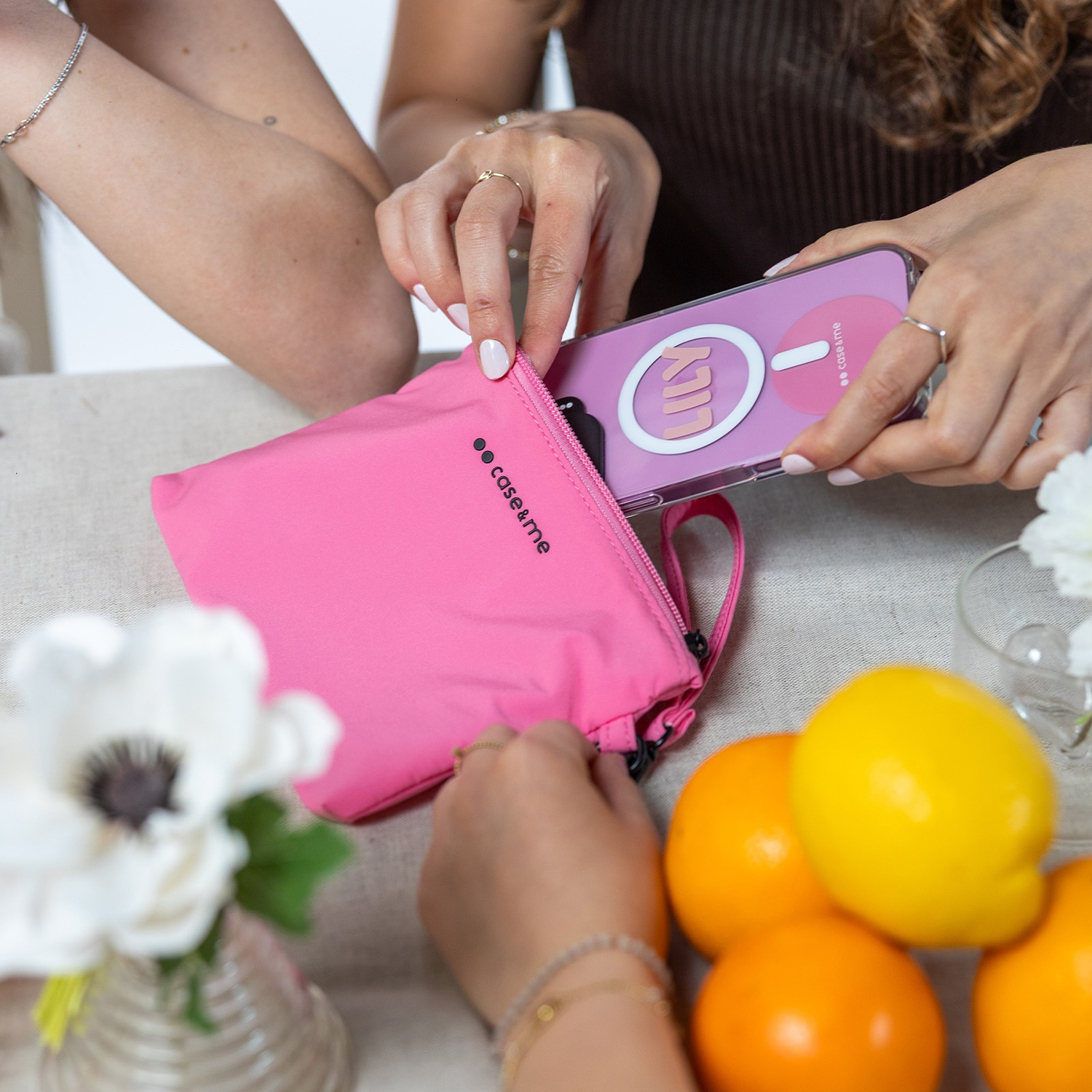 Manos metiendo un teléfono morado en un bolso rosa. Hay naranjas cerca.