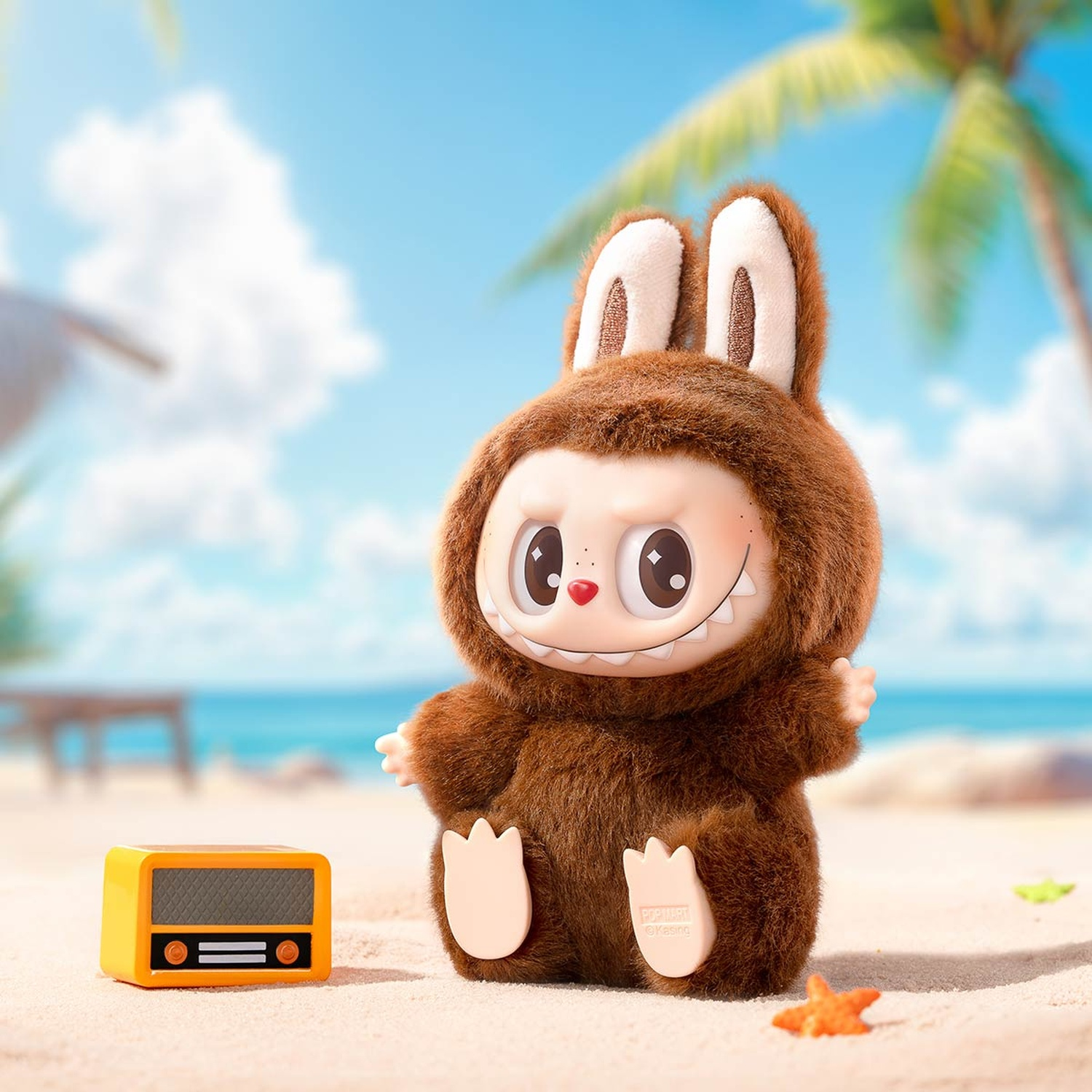 Brauner Plüschhase mit Ohren sitzt am Strand neben einem gelben Radio.
