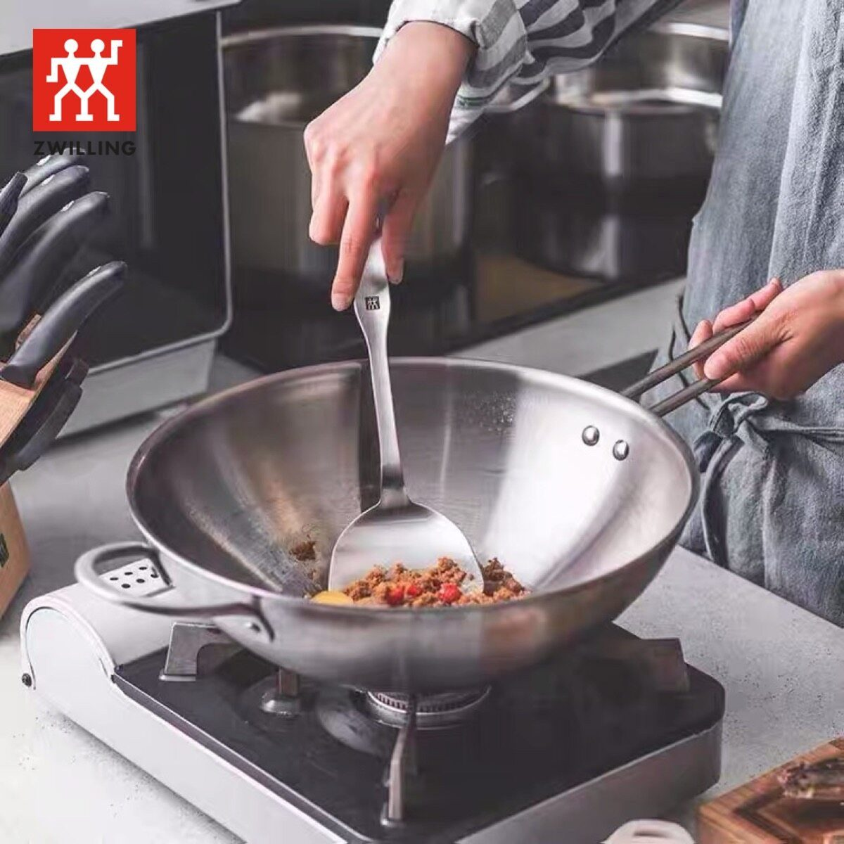Eine Person rührt Hackfleisch in einem Wok mit einem Spatel. Zwilling-Logo sichtbar.