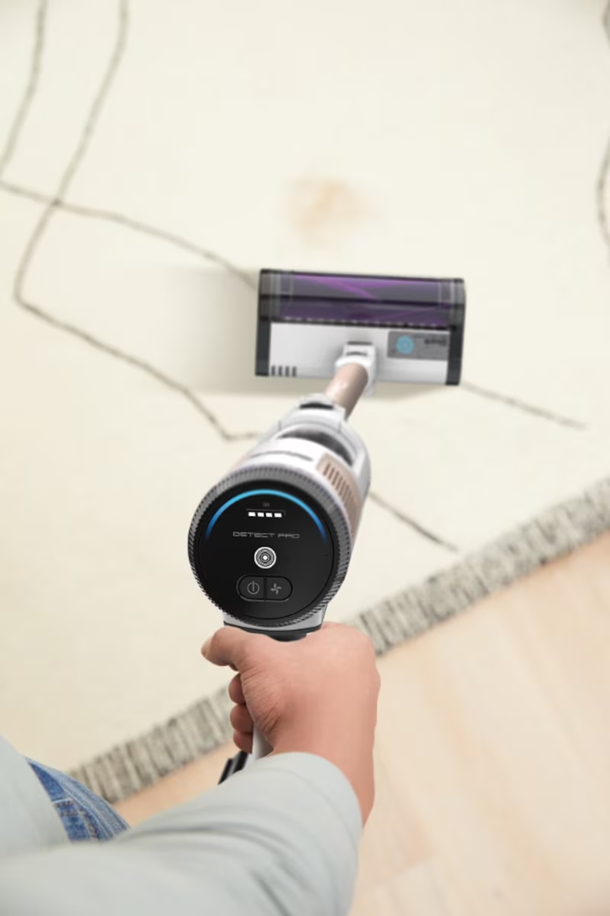 Hand holding vacuum with display and brush over light rug.