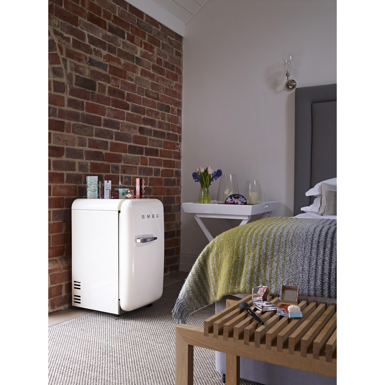 Una nevera Smeg blanca junto a una pared de ladrillos en un dormitorio.