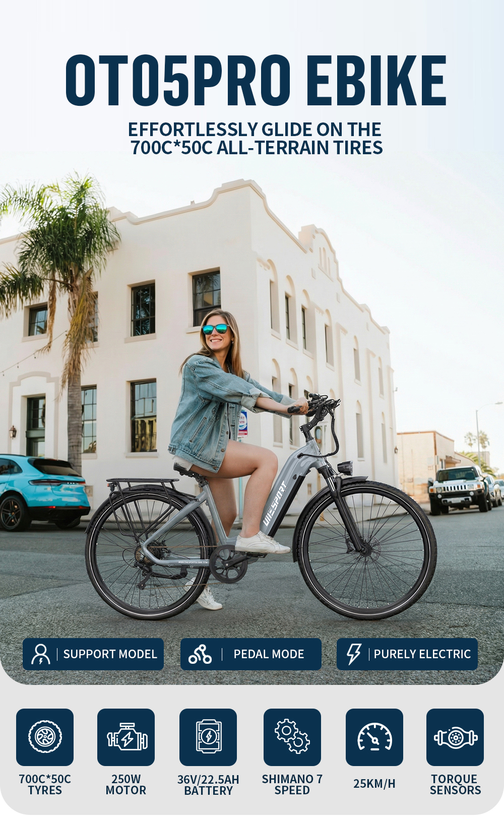 Una donna guida una e-bike grigia davanti a un edificio bianco e palme.
