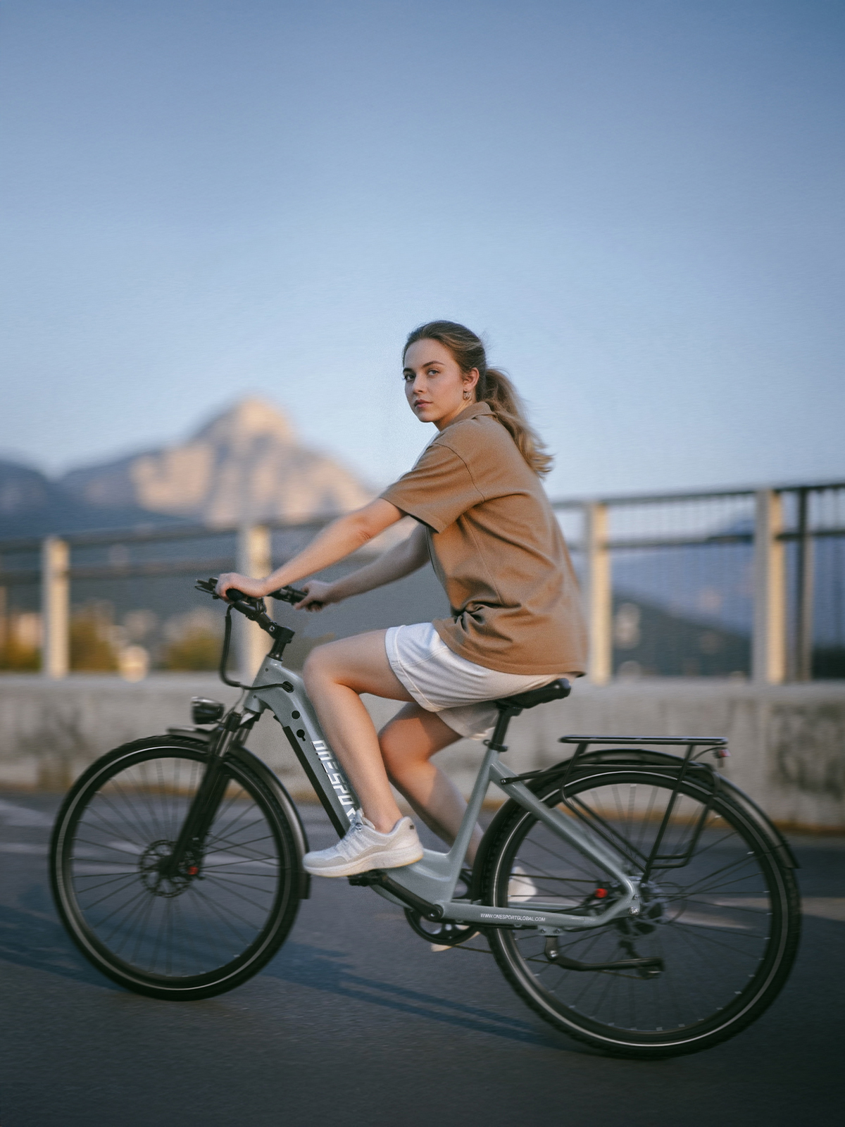 Una mujer monta una bicicleta gris frente a una montaña y cielo azul.