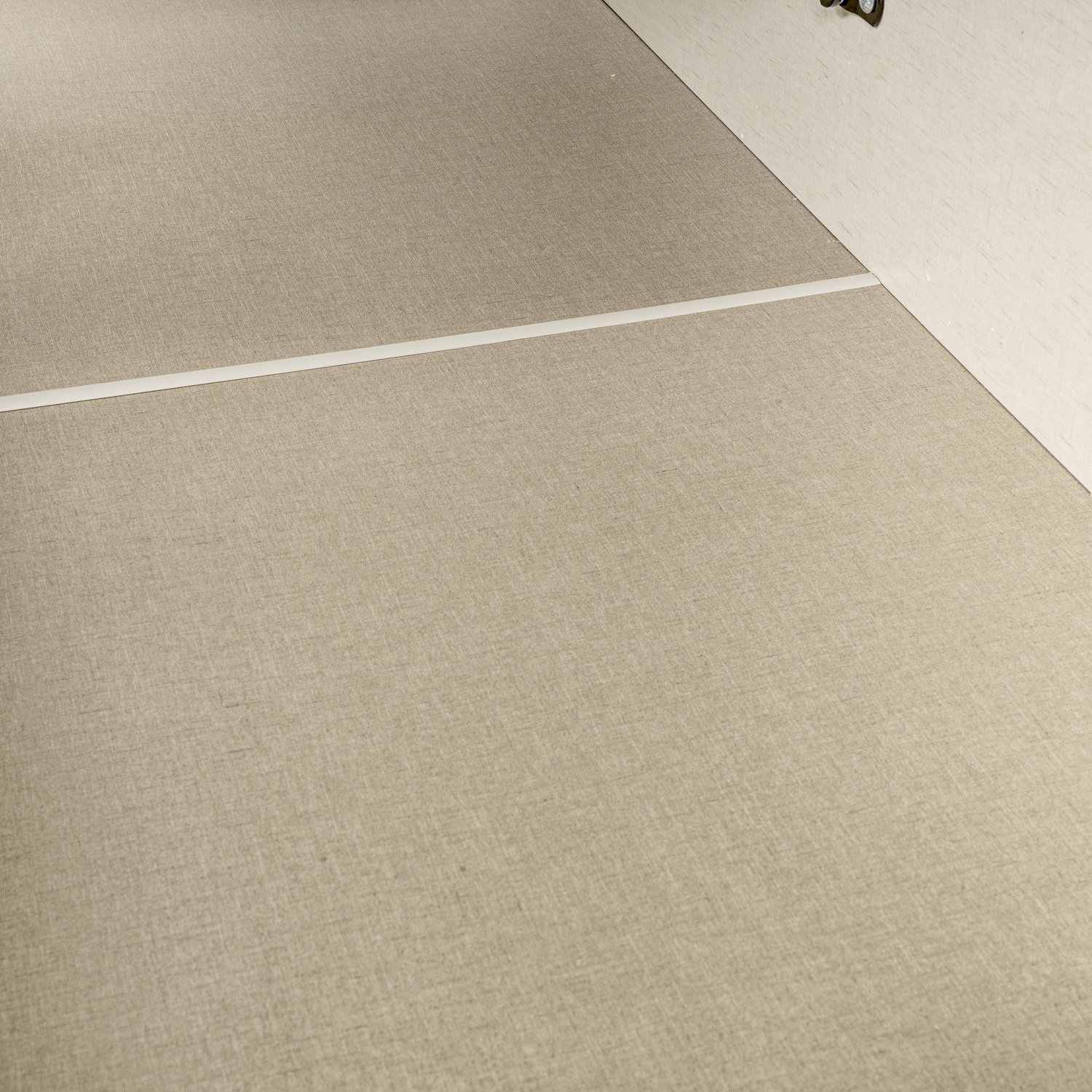 Alfombra beige con raya blanca, junto a una pared clara.