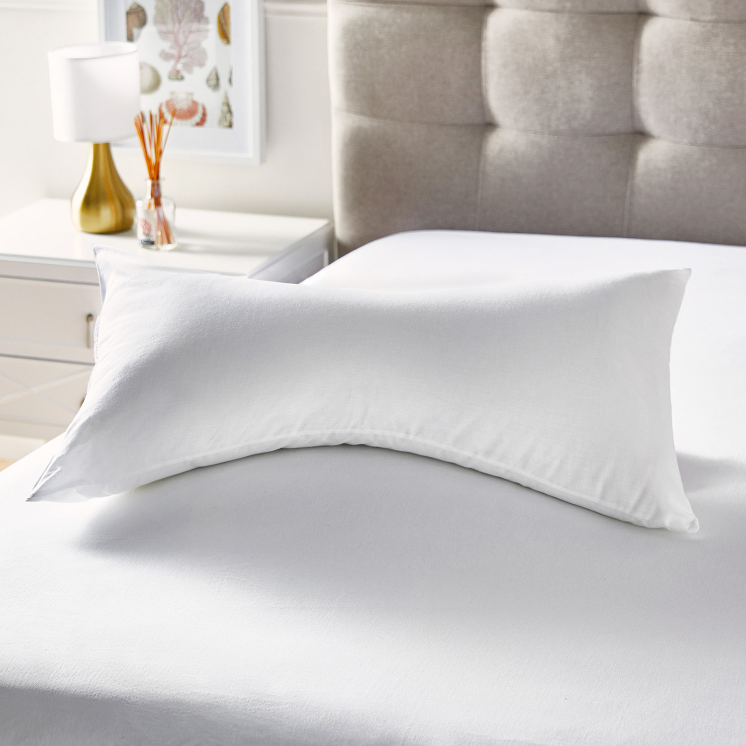 Una almohada blanca descansa sobre una cama blanca, con una mesita de noche cerca.