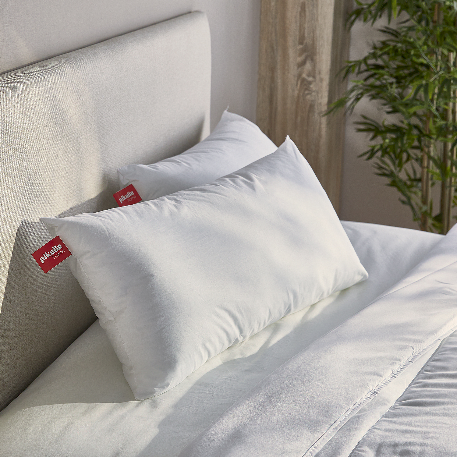 Dos almohadas blancas sobre una cama con cabecero y bambú al fondo.
