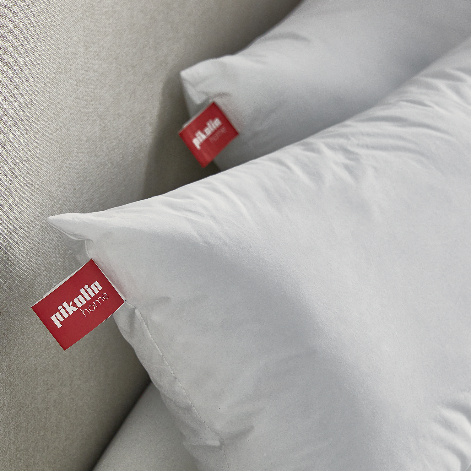 Dos almohadas blancas descansan sobre un fondo gris texturizado. Se ve una etiqueta roja.
