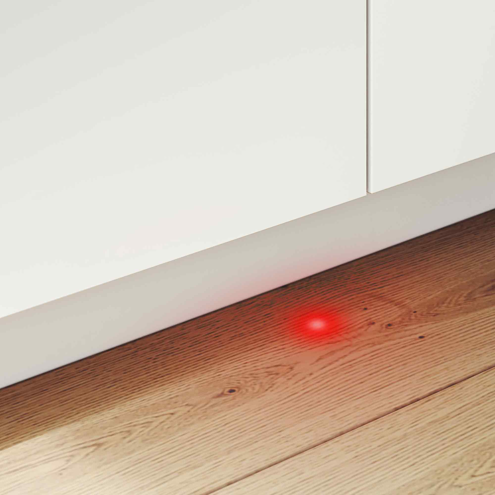 Ein roter Punkt leuchtet auf einem Holzboden neben einer weißen Wand.