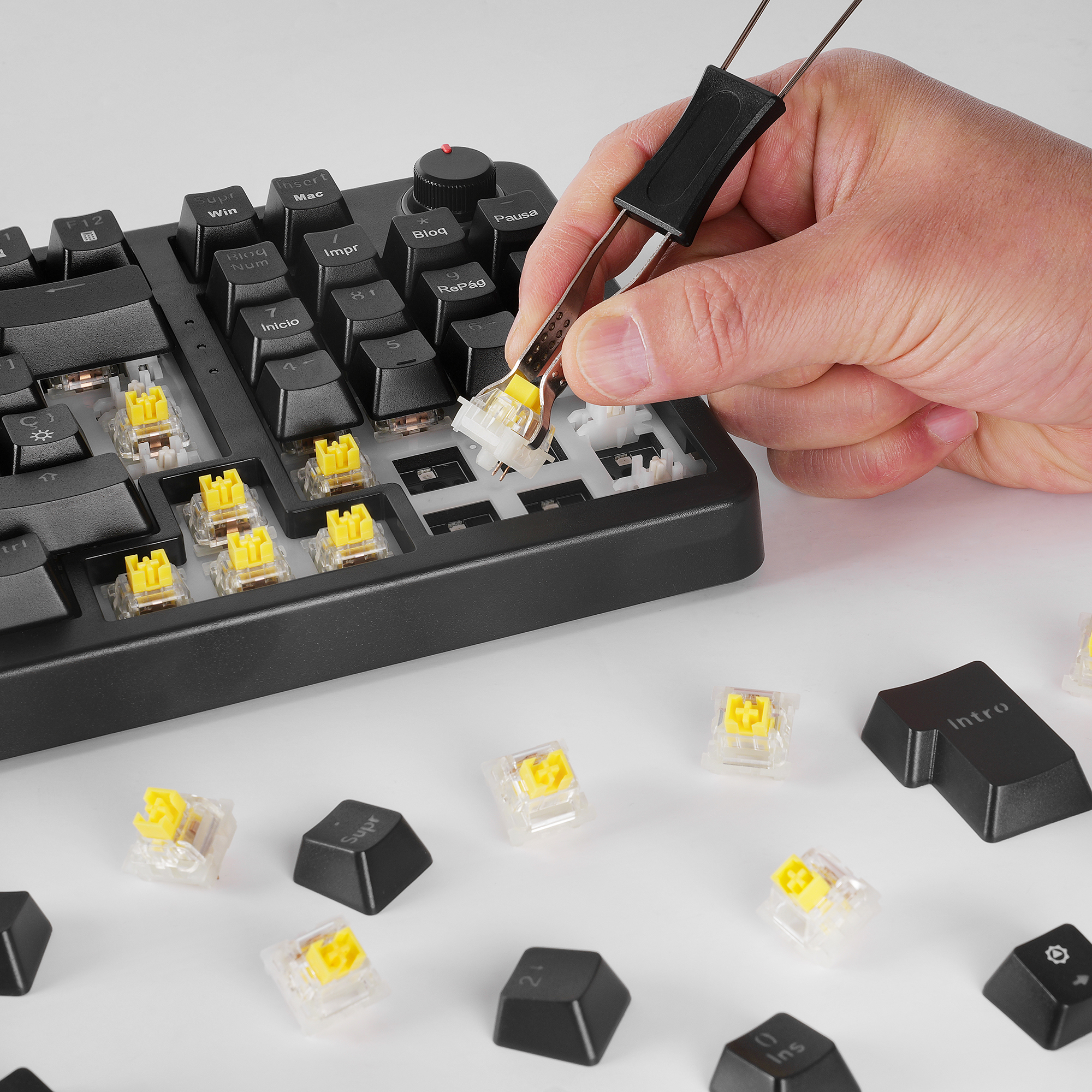 Una mano usa pinzas para quitar un interruptor de tecla amarillo de un teclado.