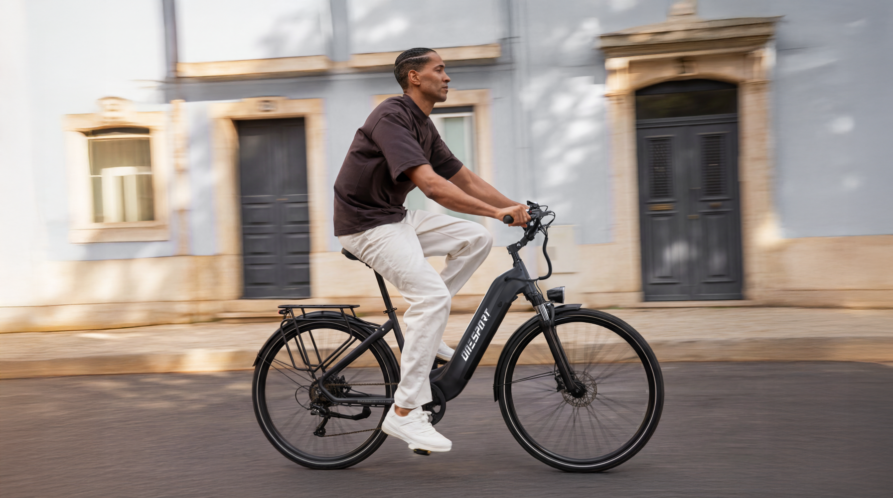 Un hombre monta una bicicleta eléctrica negra en una calle frente a un edificio azul.