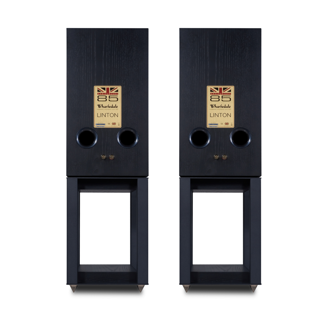 Twee zwarte luidsprekers met gouden logo's, op donkere standaards.