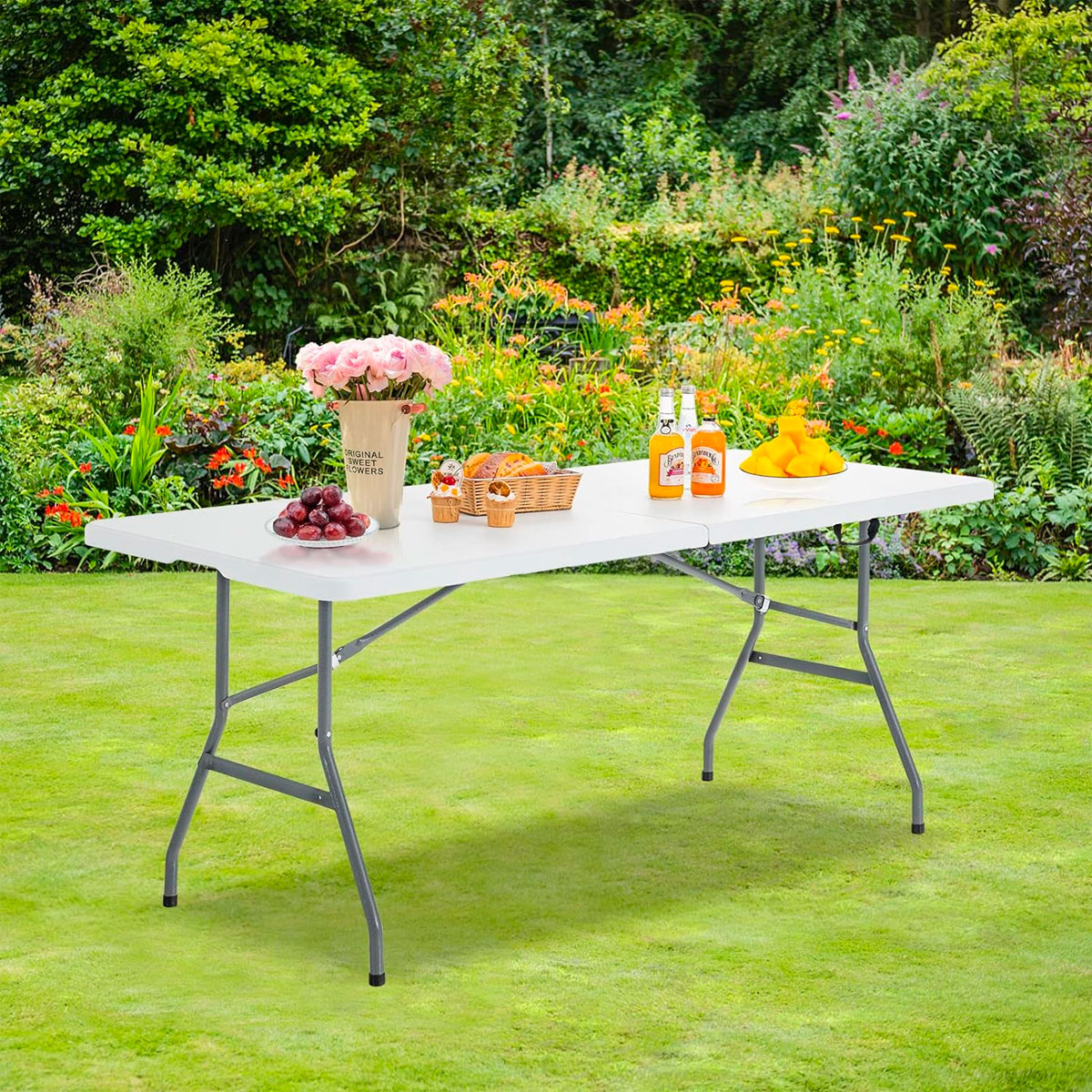 Una mesa plegable blanca con aperitivos y bebidas en un jardín.