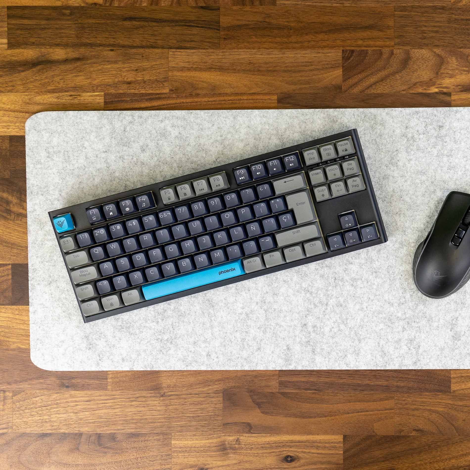 Teclado negro con teclas azules sobre fieltro gris, junto a un ratón negro.